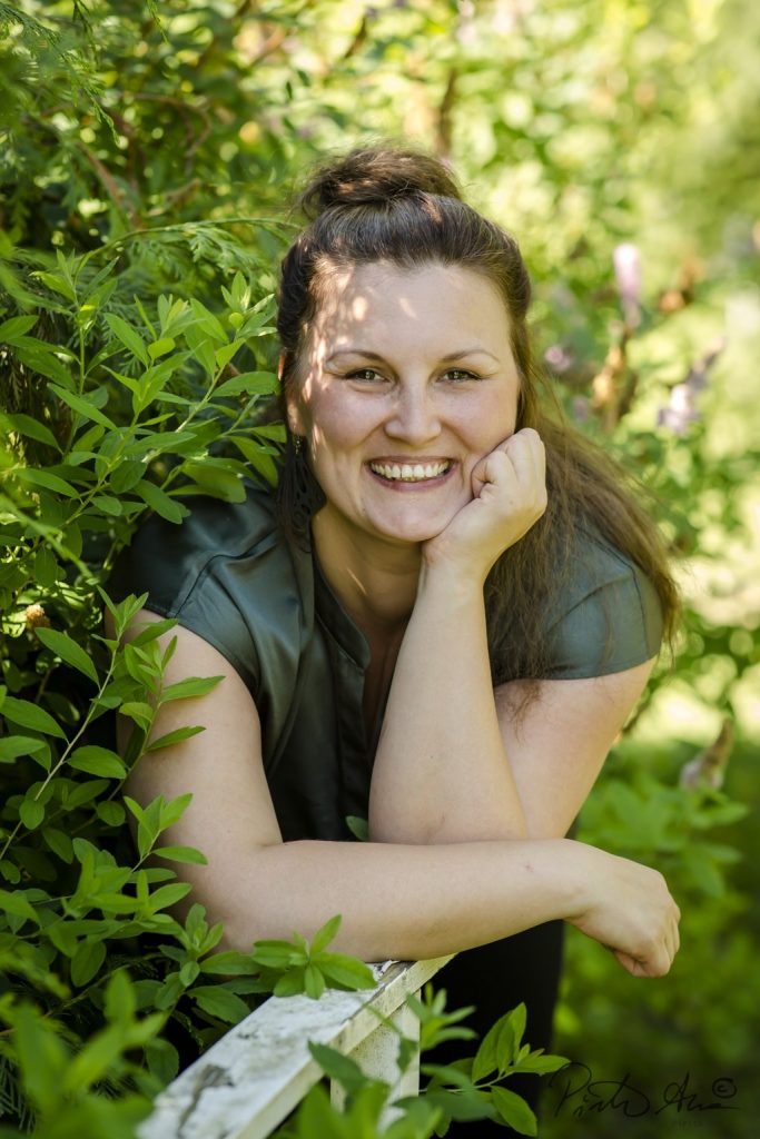 Laura Elonen hymyilee vihreä paita päällä vihreän luonnon keskellä.