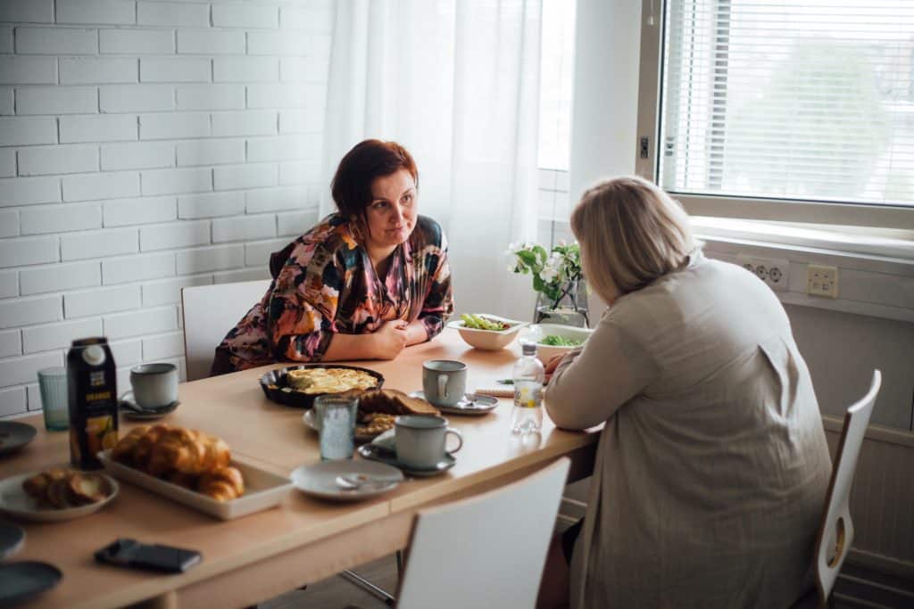 Laura istuu kollegansa kanssa kahvipöydässä keskustelemassa.